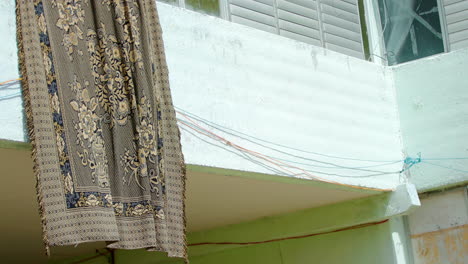 large rug hanging outside building drying in the sun and fluttering in wind in cuba