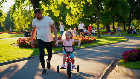 father teaching daughter to ride a tricycle in a park