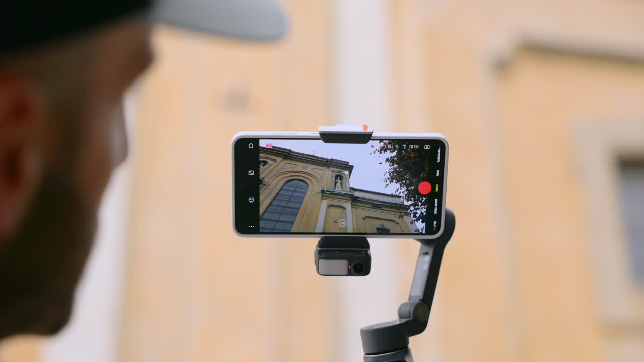 Primo piano di uno smartphone su un gimbal portatile mentre un uomo tocca lo schermo per filmare la facciata di un edificio storico