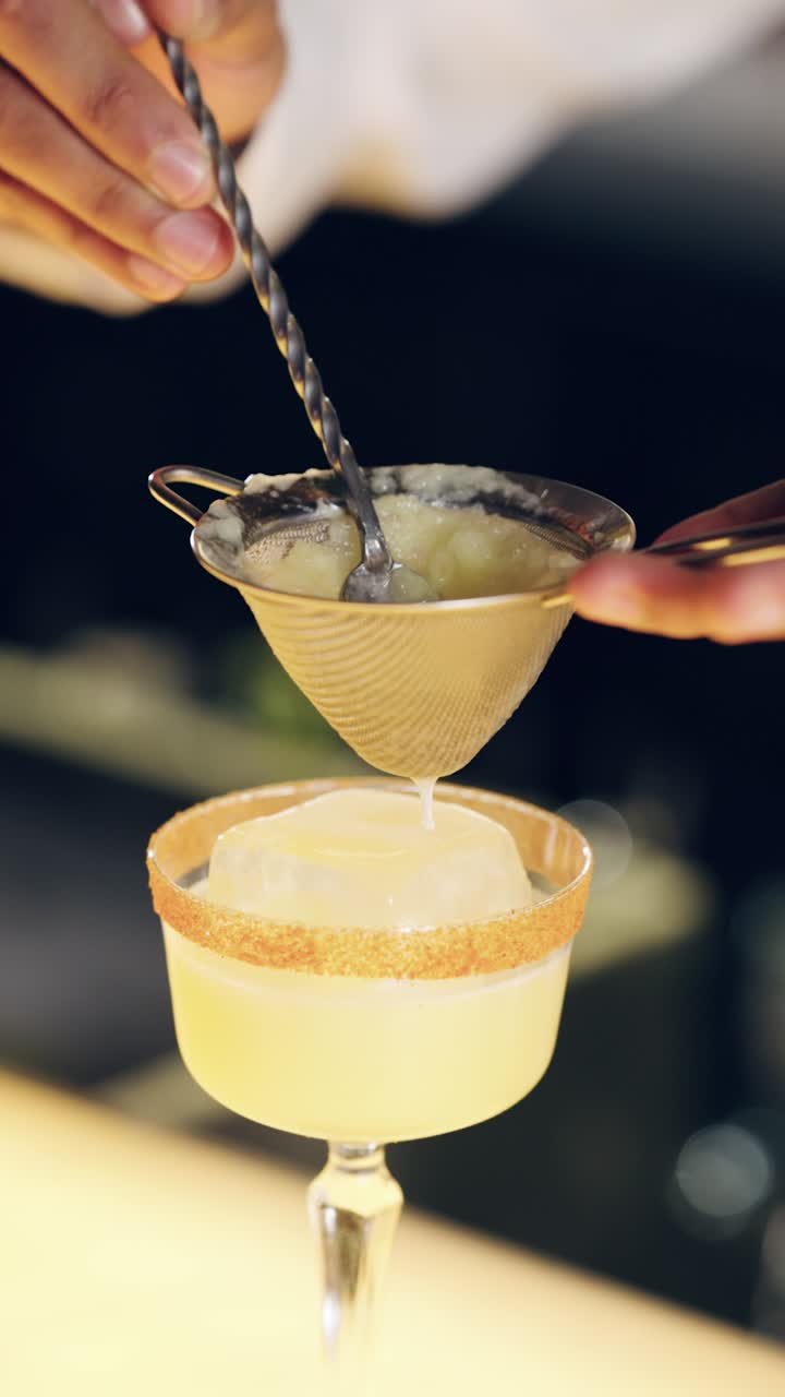 Barman che filtra un cocktail artigianale in un bicchiere con ghiaccio