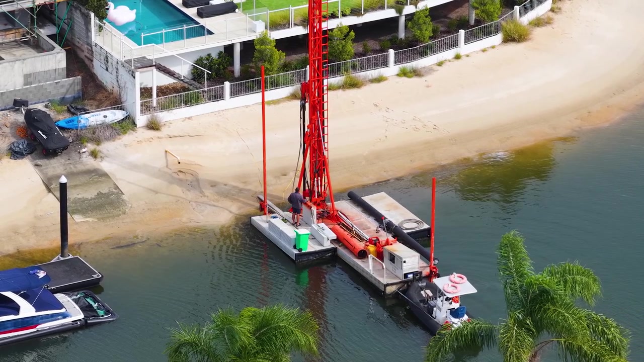 High angle aerial shot of a red piling rig operating on a residential canal waterfront