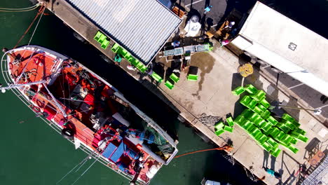 elevador aéreo por encima de un buque pesquero amarrado en la pared del puerto descargando su captura