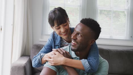 Portrait-of-happy-diverse-couple-sitting-on-couch-and-embracing-in-living-room