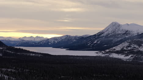 a breathtaking sunset over the frozen takhini river and kusawa lake in yukon reveals snow-covered landscapes, fir forests, and mountains. this serene winter scene captures dramatic twilight.