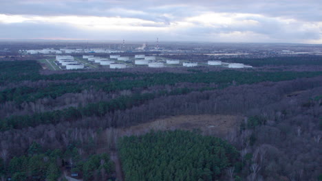 Vuelo-Aéreo-Más-Allá-Del-Paisaje-Forestal-Con-Tanques-De-Almacenamiento-De-Aceite-Industrial-En-Segundo-Plano