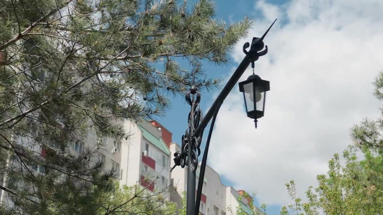 Farola ornamentada contra el cielo azul con pinos y un edificio residencial