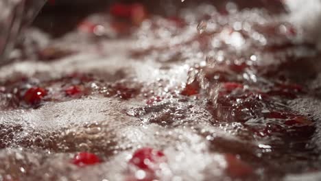 a plastic crate of fresh strawberries being poured into bubbling water for cleaning in a factory