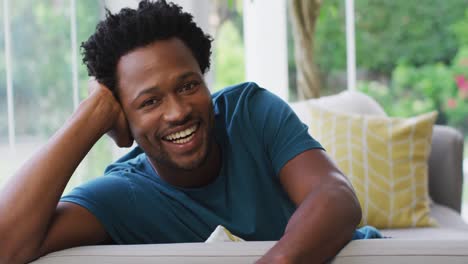 portrait of biracial man sitting on sofa and smiling to camera