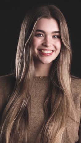 happy young woman standing in light against dark wall