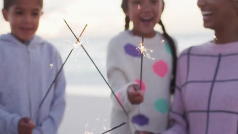 Happy-hispanic-mother,-daughter-and-son-playing-with-sparklers-on-beach