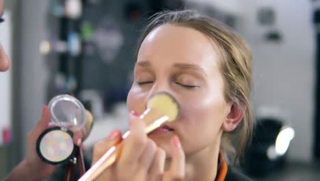 make-up artist doing make-up accents using shiny shadows. putting on the face, nose using fingers and a brush. make up studio