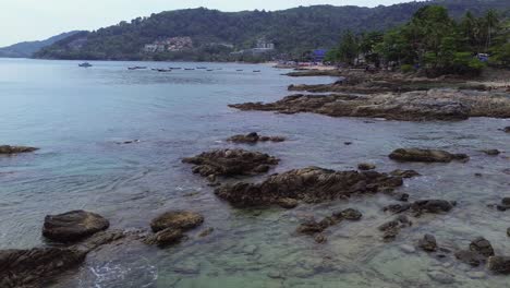 drone flight at low altitude panning left over clear water and rocky shore in phuket