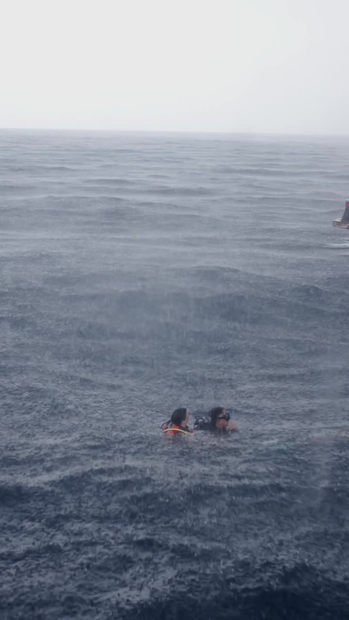 People swimming in the ocean during a rainstorm near a boat