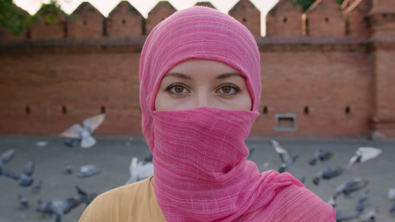 Donna con hijab rosa davanti a un muro di mattoni