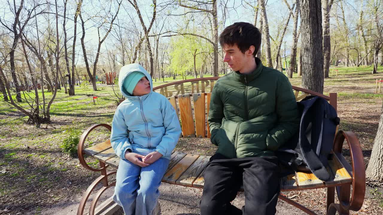 Young Man and Boy Chatting on a Bench in a Sunny Park