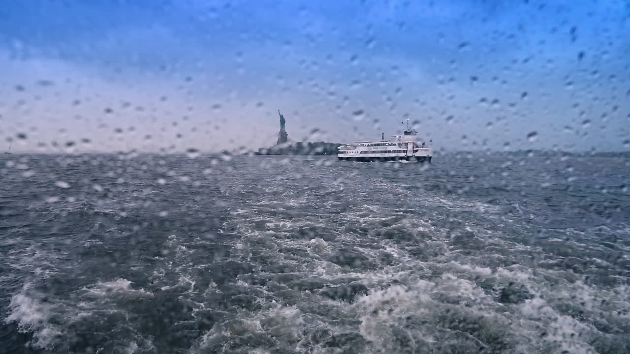 View through the window covered with multiple water drops on the boat moving by the waterscape. Another riverboat and Statue of Liberty at backdrop