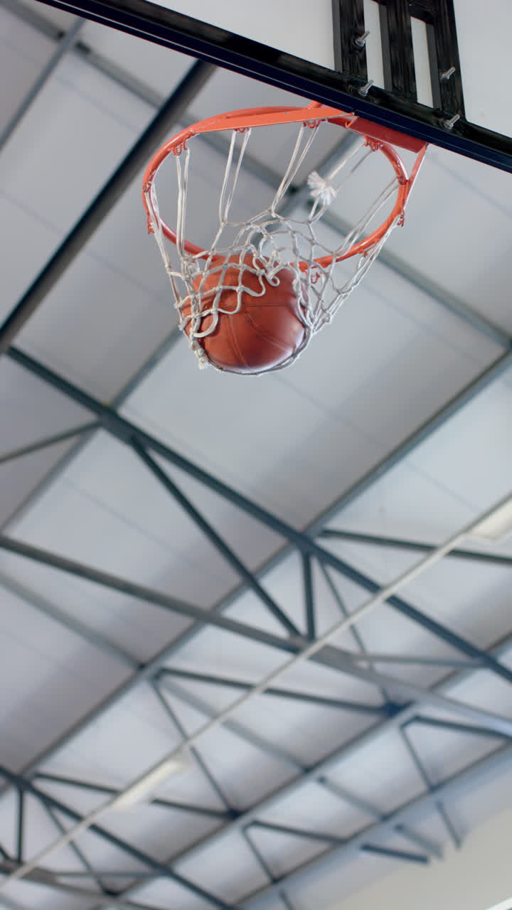 Vertical video: Scoring point, basketball going through hoop in indoor gym