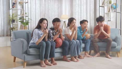 asian teenagers cheering and watching basketball game on tv at home