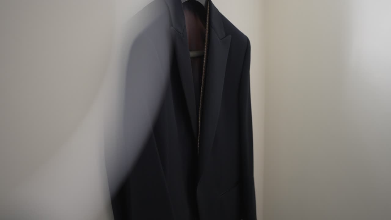 Black suit on a wooden hanger against a neutral background, minimalistic and formal
