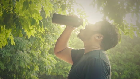 young man hydrating his body by drinking water from a bottle during workout at outdoor nature