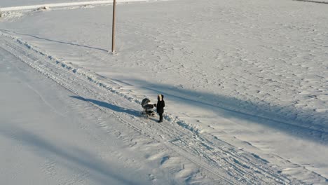 Aerial-view-of-woman-stand-on-snowy-countryside-road-near-baby-carriage