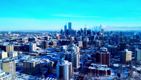 winter snow covered residential commercial high rises with steam coming our of their chimney's during an extreme winter cold weather aerial pan from downtown west to south on clear sunny afternoon