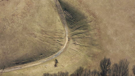 an aerial top down shot over an open field with a ridge covered by dry grass, taken on a sunny day