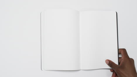 Video-of-hand-of-african-american-man-holding-book-with-blank-pages,-copy-space-on-white-background