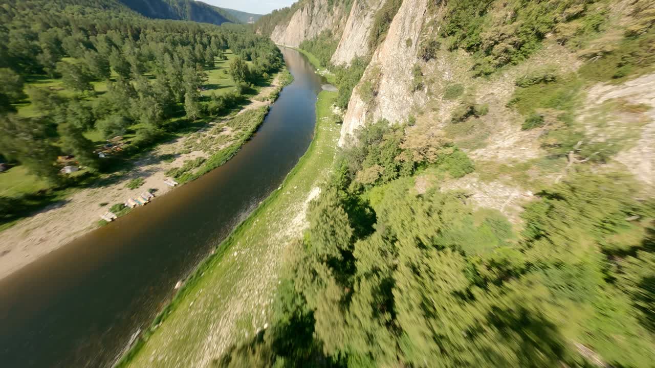 el descenso empinado por la ladera de la montaña hasta el río. los árboles proyectan largas sombras en el suelo. los catamaranes se encuentran en pequeñas playas de arena a lo largo de la orilla del río.