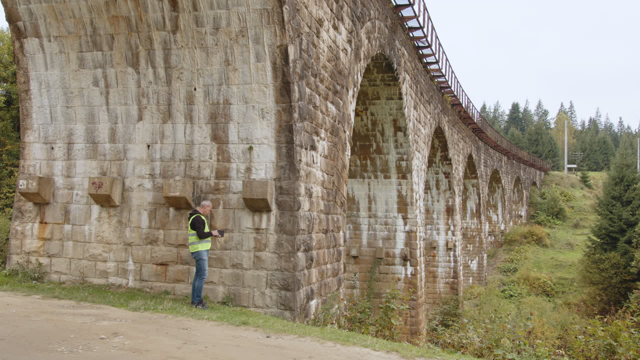 가을의 숲에서 돌로 된 아치 철도 다리를 점검하는 엔지니어