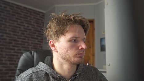 a young man with disheveled hair looks into the computer monitor and expresses concern over what he sees