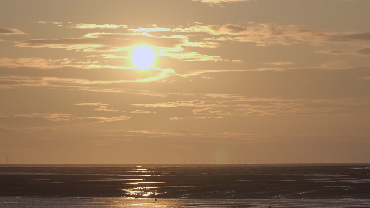 золотое солнце опускается за облаком на закате с ветряной фермой на горизонте