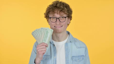 redhead young man holding dollars, yellow background
