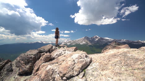 young woman on top of summit with stunning view of rocky mountains on sunny summer day, colorado usa, tilt down, full frame