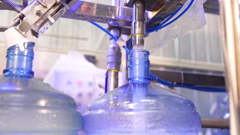 clean water is filling the big blue bottle from a metal tube. water overflows the flask. close up.