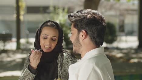 Side-view-of-young-muslim-couple-eating-lunch-in-park.