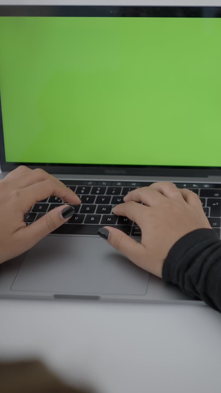 Close-up of hands typing on a laptop with a green screen
