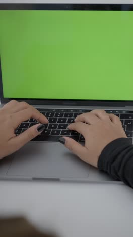 close-up of hands typing on a laptop with a green screen