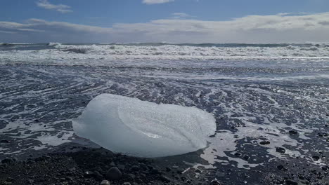 glacier ice on black beach in front of sea waves, global warming and climate change concept