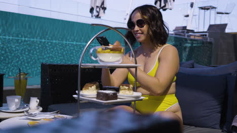 slow motion shot of a female in a bikini taking photos of expensive cakes and sandwiches