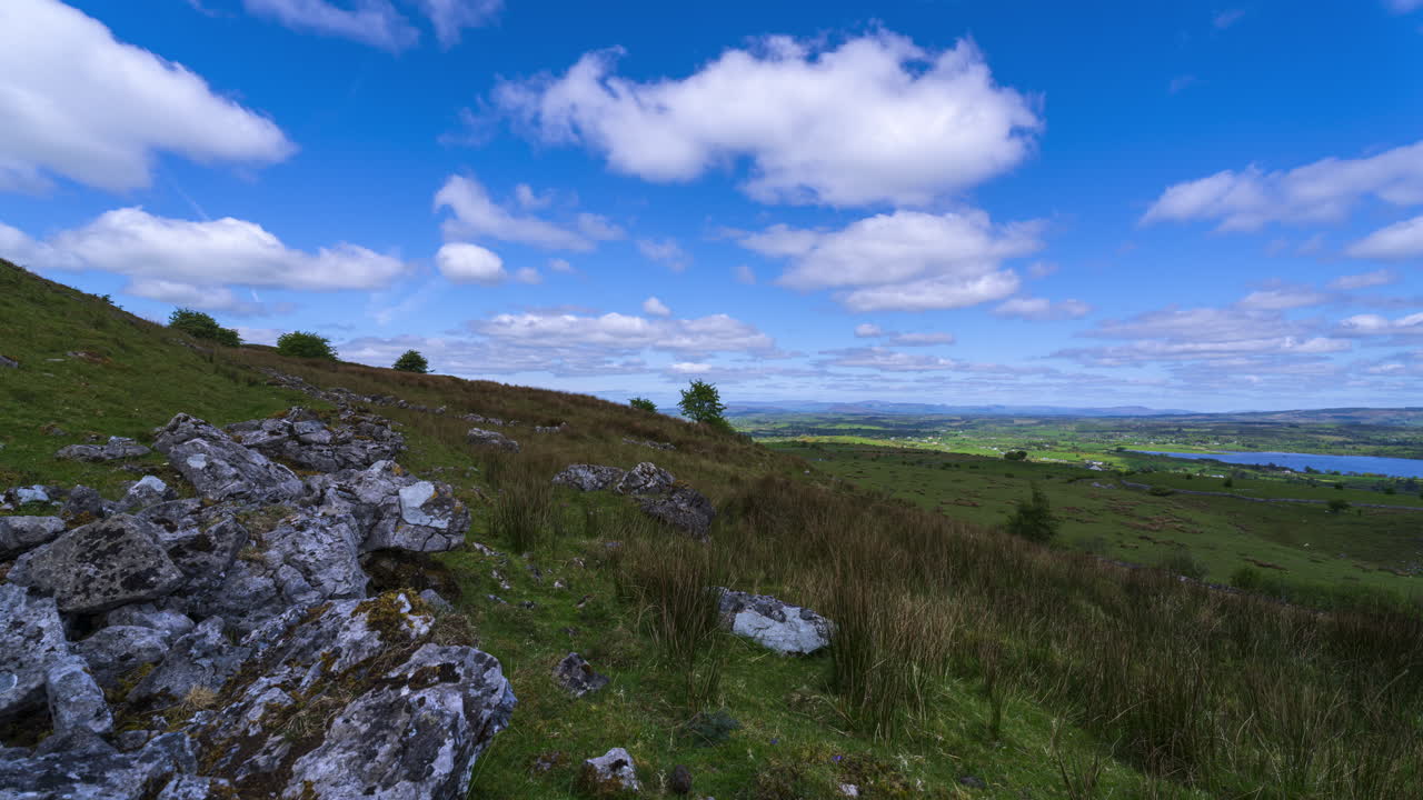 Timelapse panoramico di un paesaggio rurale con una formazione rocciosa in primo piano, colline e un lago in lontananza durante una giornata soleggiata e nuvolosa, visto da Carrowkeel nella contea di Sligo, in Irlanda