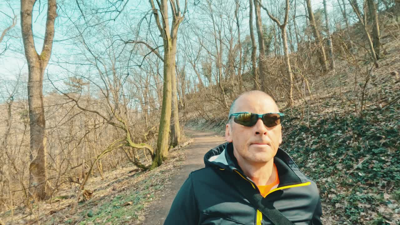Modern mature man using headphones to listen to an educational podcast or music while walking in nature. Intersection of technology and wellness in senior years