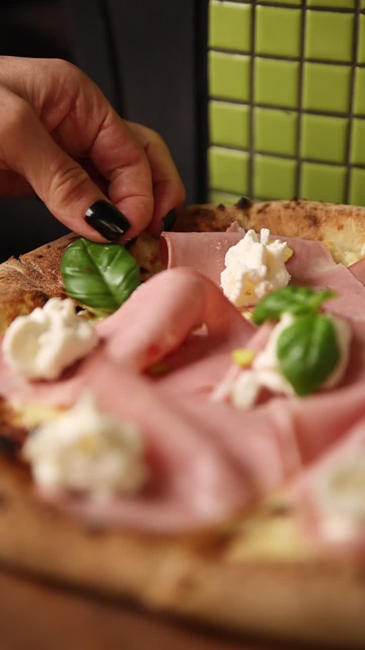 Mano che posiziona una foglia di basilico fresco su una deliziosa pizza al prosciutto e formaggio