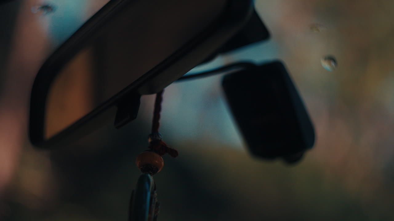 A cinematic close-up of a vehicle's rearview mirror reflecting the road and trees during a road trip, featuring soft natural light
