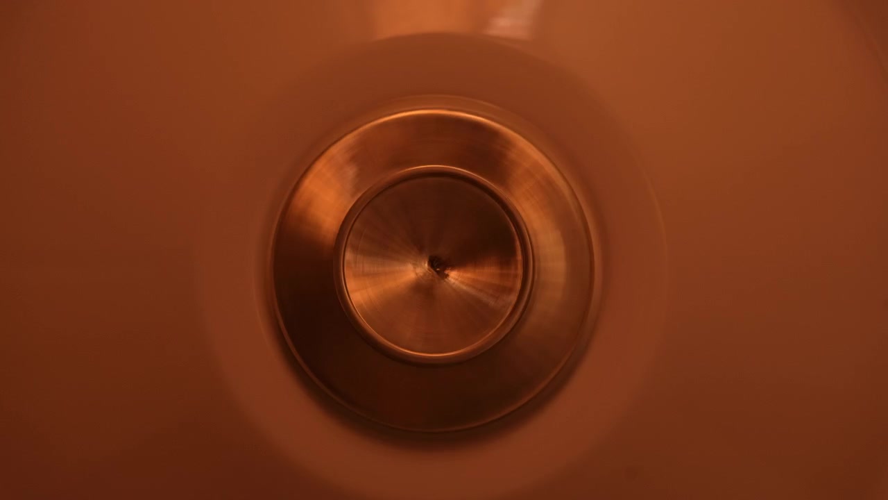 Close-up of a circular metal fixture centered against a warm orange surface, rotating gyrating spinning from motion of fan