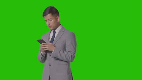 foto de estudio de un hombre de negocios con traje mirando un teléfono móvil contra una pantalla verde