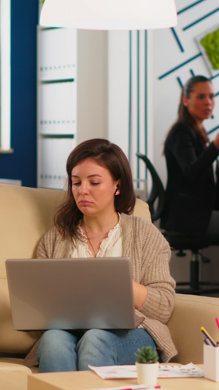 Vertical video Manager woman sitting on couch holding laptop and talking on video call