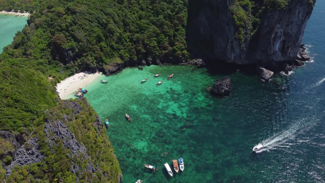 Drone shot of a hidden lagoon near Koh Phi Phi with boats floating in clear turquoise water, surrounded by coral reef and dramatic cliffs covered in dense green vegetation.