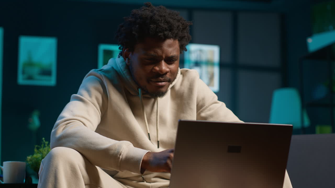 Young male freelancer managing schedules and notes on his laptop while seated in a contemporary living room. Inspiring man looks at pc for a productive teleworking session. Camera A.