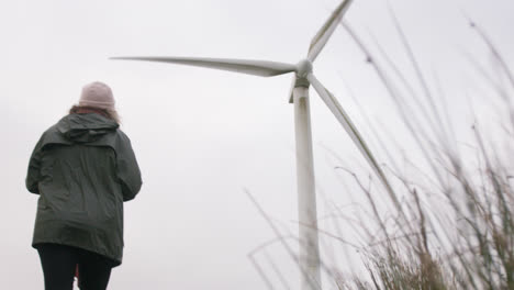 female walks across english countryside and hills with wind turbines